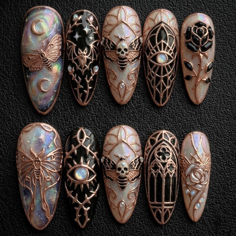 May include: A collection of ten long, oval-shaped artificial nails. Each nail showcases detailed designs, such as moths, bats, roses, and geometric patterns, in black, white, and iridescent hues, with copper-coloured metal accents.