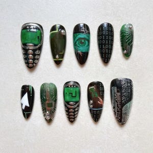 May include: A set of ten press-on nails featuring a digital technology theme. Designs include a retro mobile phone, green circuit board patterns, a human eye, binary code, a white computer cursor, and a question mark icon on a green screen.