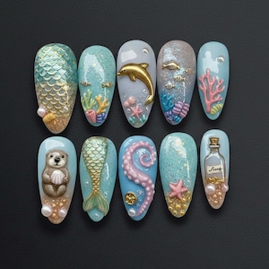Può includere: Un set di dieci unghie a mandorla dipinte con un tema oceanico. I disegni includono una coda di sirena, un delfino dorato, un polpo e una lontra. I colori includono blu, oro, rosa e bianco, con glitter e perle.
