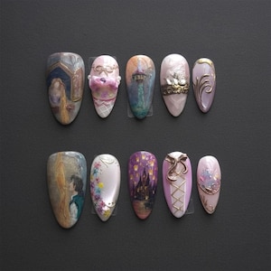 May include: A set of ten artificial nails with various designs. The designs include painted scenes, floral accents, and 3D embellishments. Colors include gold, pink, purple, and blue. The nails are arranged on a dark gray surface.