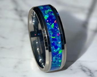 May include: A silver-toned ring with a vibrant blue opal inlay. The opal features flecks of green, pink, and blue, set within a polished metal band. The ring is a piece of jewelry.