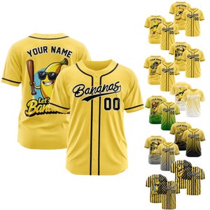 Op de afbeelding: Geel honkbalshirt met zwarte bies en het woord "Bananas" in script. Het nummer "00" staat onder het woord. Een cartoon banaan met zonnebril en een honkbalknuppel staat op de achterkant.