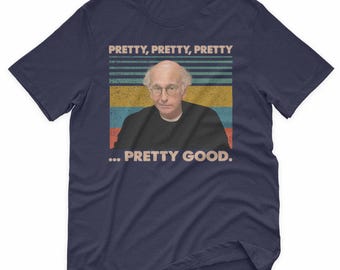 May include: Navy blue t-shirt featuring a graphic of a man with glasses and the text "PRETTY, PRETTY, PRETTY... PRETTY GOOD." The design has a retro, vintage style with horizontal stripes in various colors.