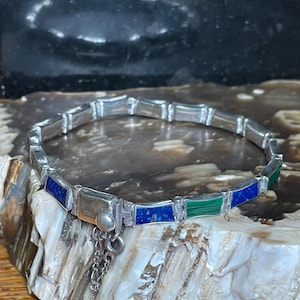 May include: A silver link bracelet featuring alternating rectangular inlays of deep blue lapis lazuli and vibrant green malachite. The bracelet includes a secure box clasp mechanism with a small attached safety chain for added security during wear.
