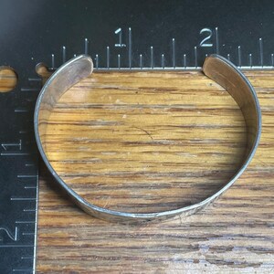 May include: A silver cuff bracelet with a hammered texture. The bracelet is approximately 2 inches in diameter and has a simple, classic design. The metal has a slightly tarnished appearance, giving it a vintage feel.