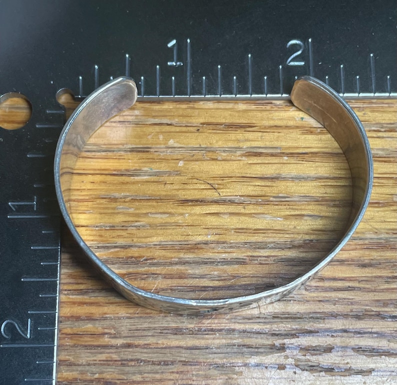 May include: A silver cuff bracelet with a hammered texture. The bracelet is approximately 2 inches in diameter and has a simple, classic design. The metal has a slightly tarnished appearance, giving it a vintage feel.