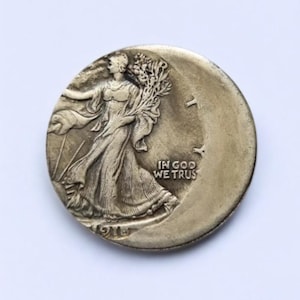 May include: A silver coin featuring a woman walking towards the left, carrying branches, with the text "IN GOD WE TRUST". The coin has a crescent moon shape on the right side and the year 1916 is visible.