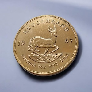 Può includere: Moneta d'oro Krugerrand del 1967, raffigurante un'antilope springbok. La moneta è incisa con "KRUGERRAND", "FYNGOUD 1 OZ FINE GOLD" e l'anno. La moneta ha un bordo strutturato ed è un prezioso oggetto da collezione.
