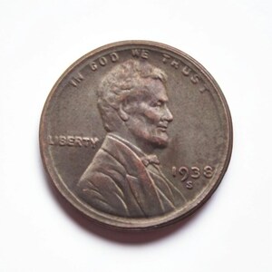 Op de afbeelding: Een koperkleurige 1938 S Lincoln cent munt. De voorzijde toont een profiel van Abraham Lincoln, het woord "LIBERTY" en de inscriptie "IN GOD WE TRUST". Het jaartal en het muntteken zijn ook zichtbaar.