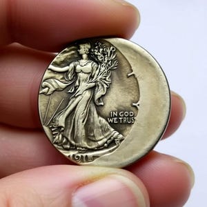 May include: A silver coin with a detailed relief of a woman walking, holding branches, and the text "IN GOD WE TRUST". The coin is dated 1916 and has a crescent shape cut out of it.