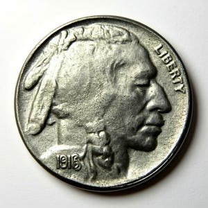 May include: A silver-colored coin featuring a profile of a Native American man with the word "LIBERTY" and the year "1916" visible. The coin has a detailed design and a slightly worn appearance.