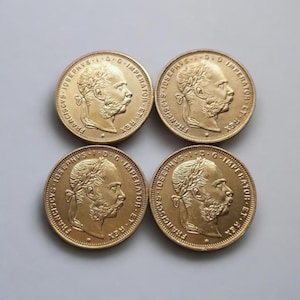 Könnte beinhalten: Vier goldfarbene Münzen mit detaillierten Reliefporträts eines Mannes im Profil, umgeben von Inschriften. Die Münzen sind quadratisch angeordnet und zeigen ihre aufwendigen Designs und historische Bedeutung.