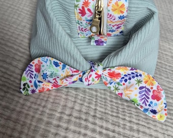 May include: A light blue corduroy cosmetic bag with a floral print accent and a gold zipper. The bag has a matching floral bow. The bag is designed for storing makeup and other beauty products.