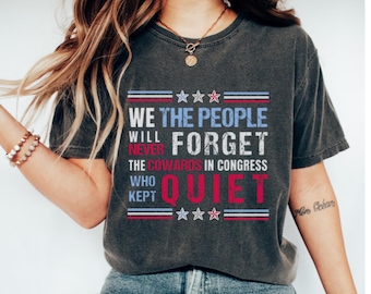 Puede incluir: Camiseta gris oscuro con el texto "WE THE PEOPLE WILL NEVER FORGET THE COWARDS IN CONGRESS WHO KEPT QUIET" en rojo, blanco y azul. El diseño incluye estrellas y rayas.