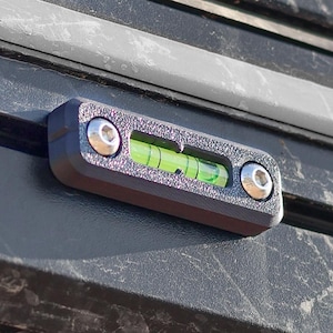 May include: A black and silver spirit level with a green liquid bubble, mounted on a dark surface. The level is secured with two silver screws. The text "M42" is visible in the lower left corner.