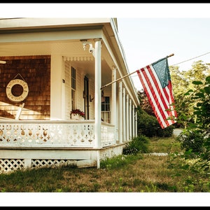 May include: A white wooden house with a porch and a white picket fence. An American flag hangs from the porch, waving in the breeze. The house has a wooden sign that reads "North Star New York".