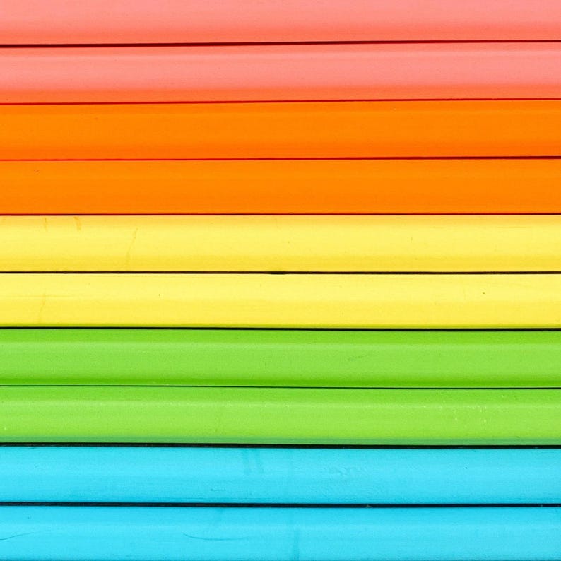 May include: A series of parallel wooden pencils arranged horizontally in a spectrum of colors. The sequence features rows of coral, orange, yellow, lime green, and light blue pencils, each with a smooth, matte finish and distinct dark lines.