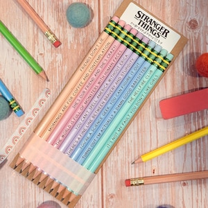 May include: A set of ten wooden pencils in a cardboard sleeve labeled Stranger Things. Each pencil features a unique pastel color and is engraved with a quote from the show, including Friends Don't Lie and Mornings Are For Coffee And Contemplation.
