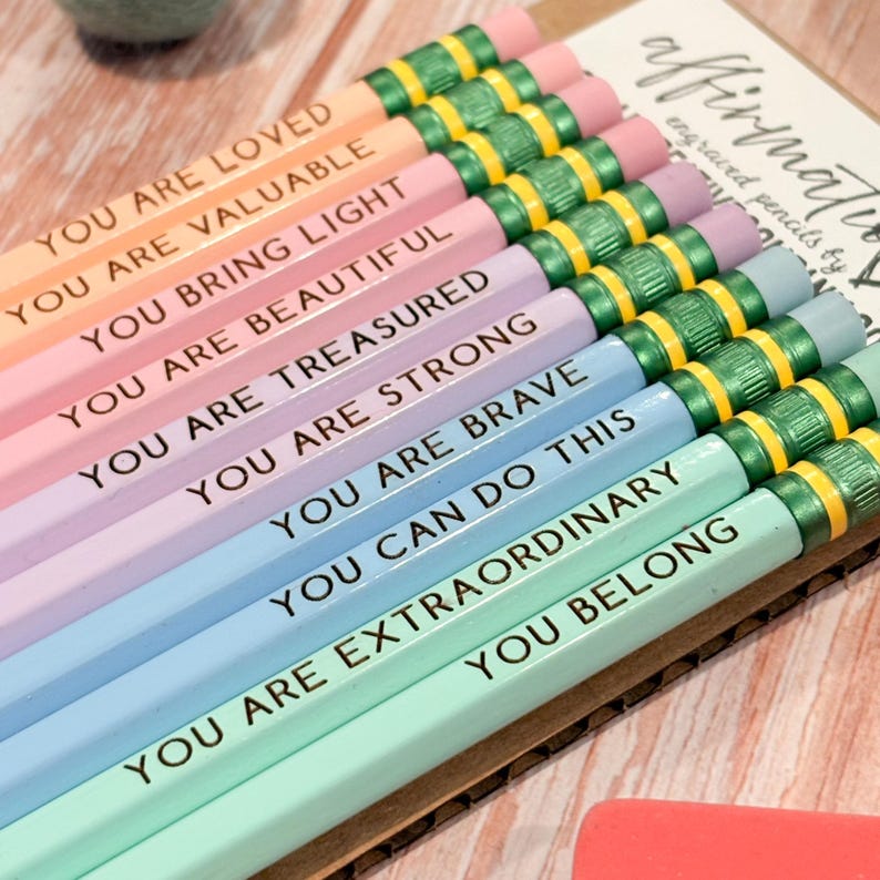 May include: A set of ten pastel-coloured pencils arranged in a row, each featuring a unique positive affirmation printed in black text. The pencils have metallic green ferrules and pink erasers, with phrases including You Are Loved, You Are Valuable, You Bring Light, You Are Beautiful, You Are Treasured, You Are Strong, You Are Brave, You Can Do This, You Are Extraordinary, and You Belong.