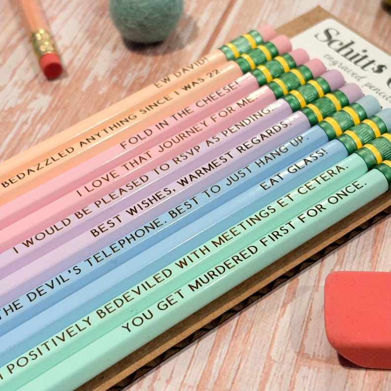 May include: A set of pastel-colored pencils with green ferrules and pink erasers, each engraved with quotes including EW DAVID, FOLD IN THE CHEESE, I LOVE THAT JOURNEY FOR ME, I WOULD BE PLEASED TO RSVP AS PENDING, BEST WISHES, WARMEST REGARDS, EAT GLASS.