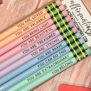 May include: A set of ten pastel-coloured pencils with green metal ferrules and pink erasers. Each pencil features black text: YOU ARE LOVED, YOU ARE VALUABLE, YOU BRING LIGHT, YOU ARE BEAUTIFUL, YOU ARE TREASURED, YOU ARE STRONG, YOU ARE BRAVE, YOU CAN DO THIS, YOU ARE EXTRAORDINARY, and YOU BELONG.