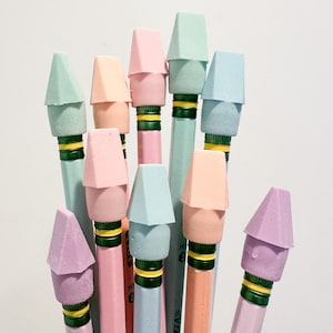 May include: A collection of pastel-colored pencils with matching erasers. The pencils are in shades of pink, blue, green, and peach. Each pencil has a green and gold band near the eraser.