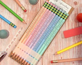 May include: A set of ten pastel-colored pencils arranged on a cardboard backing labeled Biblical Affirmations. Each pencil features a unique religious quote and scripture reference. The pencils are held together by a translucent band.