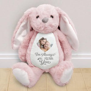 Könnte beinhalten: Ein rosa Plüschkaninchen mit langen Ohren und einer grauen Nase. Das Kaninchen hat einen weißen herzförmigen Aufnäher auf der Brust mit einem Foto und dem Text "I'm Always With You".