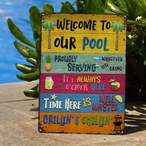 May include: A rectangular, multi-colored metal sign with the text "WELCOME TO OUR POOL". The sign has a rustic, weathered appearance and features various phrases and illustrations related to a pool and leisure, including a pineapple and a cocktail.