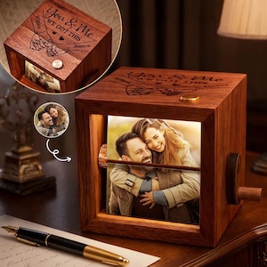 May include: A wooden music box with a photo of a couple inside. The box is engraved with the words "You & Me WE GOT THIS" and the names "William" and "Jessica". The box has a crank on the side and a small light inside.