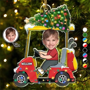 May include: A personalized Christmas ornament featuring a cartoon illustration of a person driving a red golf cart. The ornament includes a Christmas tree, golf clubs, and the name "William". The ornament is decorated with colorful lights and a photo of the person.