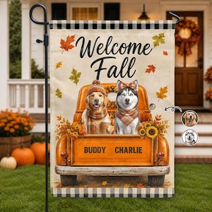 Puede incluir: Una bandera de jardín rectangular con una camioneta naranja vintage que transporta un golden retriever y un husky. El texto dice Welcome Fall y BUDDY CHARLIE. Los perros llevan bufandas y gorros a cuadros sobre un fondo de hojas de otoño.
