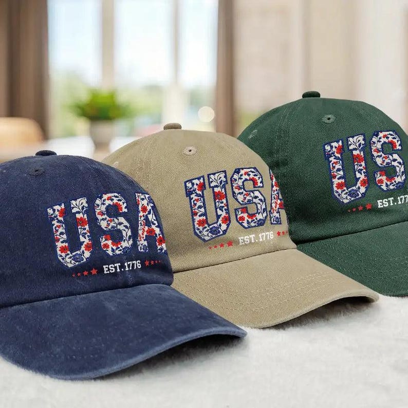 Puede incluir: Tres gorras de b&eacute;isbol en azul marino, caqui y verde. Cada gorra presenta la palabra "USA" en bordado floral, con "EST. 1776" debajo. Las gorras est&aacute;n dispuestas en fila, mostrando sus diferentes colores y dise&ntilde;os.