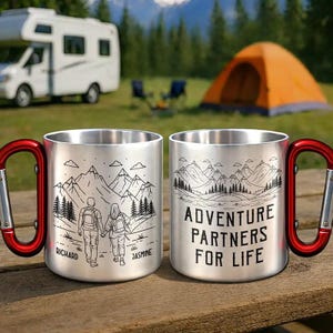 Può includere: Due tazze da campeggio in acciaio inossidabile con manici a moschettone rossi. Una tazza presenta una scena di montagna con una coppia e i nomi "Richard" e "Jasmine". L'altra tazza dice "Adventure Partners For Life".