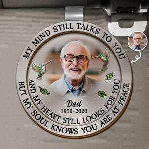 May include: A round, silver-colored memorial ornament with a photo of a smiling older man wearing glasses. The text reads "MY MIND STILL TALKS TO YOU BUT MY SOUL KNOWS YOU ARE AT PEACE." Includes hummingbirds and the text "Dad 1950-2020."