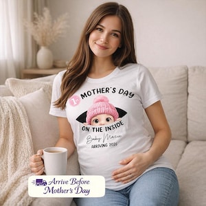 May include: White t-shirt with a graphic that reads "Mother's Day on the Inside" with a baby illustration wearing a pink hat. The text "Baby Mazie Arriving 2026" is also on the shirt. The shirt is worn by a person.