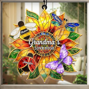 May include: A stained-glass style sunflower ornament with the text "Grandma's LOVE BUGS." The ornament features a bee, ladybug, dragonfly, and butterfly, each with a name. The sunflower has yellow, orange, and green hues.