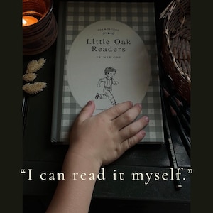 Puede incluir: Un libro de tapa dura titulado Little Oak Readers Primer One con un patr&oacute;n de cuadros vichy gris y blanco en la cubierta. La portada presenta un &oacute;valo central con una ilustraci&oacute;n en blanco y negro de un ni&ntilde;o corriendo y el texto I can read it myself.