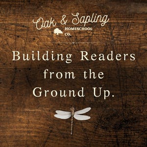 May include: A dark brown wood grain background featuring the white text Oak & Sapling HOMESCHOOL CO. with a small tree icon, followed by the text Building Readers from the Ground Up. A single dragonfly with white wings is centered at the bottom.
