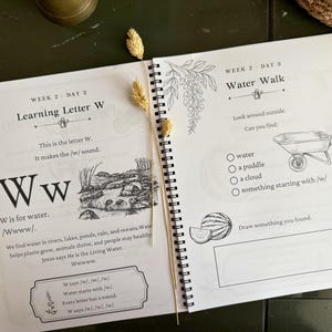 May include: A spiral-bound educational workbook open to two pages featuring lessons on the letter W. The left page includes text about the letter W, a river illustration, and a box for notes. The right page lists a Water Walk activity with a wheelbarrow illustration and a blank box for drawing.