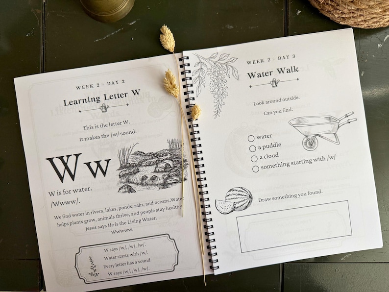 May include: A spiral-bound educational workbook open to two pages featuring lessons on the letter W. The left page includes text about the letter W, a river illustration, and a box for notes. The right page lists a Water Walk activity with a wheelbarrow illustration and a blank box for drawing.