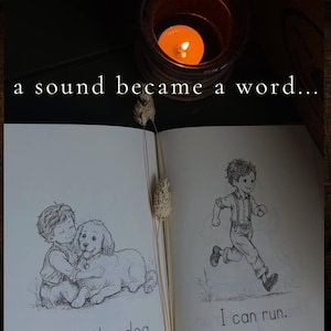 Puede incluir: Un libro abierto con ilustraciones de l&iacute;neas en blanco y negro de un ni&ntilde;o abrazando a un perro y un ni&ntilde;o corriendo, con el texto "a sound became a word..." en la parte superior y "I can run." en la inferior, iluminado por una vela.