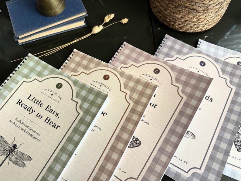 May include: A set of five spiral-bound educational workbooks with gingham patterned covers in shades of green, tan, brown, and gray. Each cover features a decorative label with the text Oak & Sapling Foundations and a detailed insect illustration.