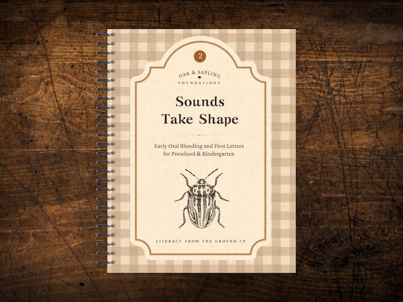 May include: A spiral-bound educational workbook with a beige and white gingham cover. The cover features the text Oak & Sapling Foundations, Sounds Take Shape, Early Oral Blending and First Letters for Preschool & Kindergarten, and Literacy From The Ground Up, with a central black and white illustration of a beetle.