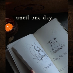 Puede incluir: Un libro abierto con ilustraciones de l&iacute;neas en blanco y negro de un insecto y un cerdo, con el texto "until one day...", "The bug" y "The pig can" impreso en las p&aacute;ginas, acompa&ntilde;ado de una peque&ntilde;a vela encendida en un portavelas.