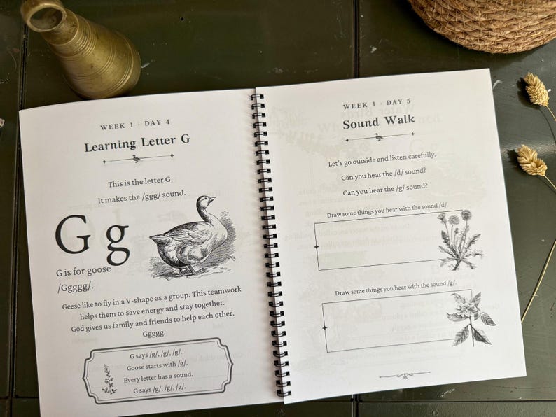 May include: A spiral-bound educational workbook open to two pages. The left page is titled Learning Letter G and features a goose illustration with text about the letter G. The right page is titled Sound Walk with prompts to draw items.