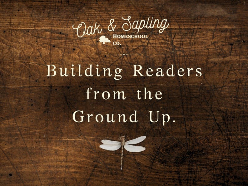 May include: A dark brown wood-grain background featuring the white text Oak & Sapling HOMESCHOOL CO. with a tree icon, followed by the text Building Readers from the Ground Up. A small, detailed dragonfly illustration is positioned below the text.