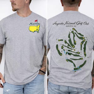 Può includere: Una maglietta grigio melange con una mappa del campo da golf sul retro e un logo Masters sul davanti. Il logo anteriore include un contorno della mappa giallo con una bandiera rossa. Il retro della maglietta mostra il logo dell'Augusta National Golf Club.