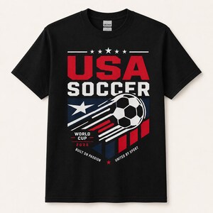 May include: Black t-shirt with a graphic design for USA Soccer. The design includes the text "USA SOCCER" in red and white, a soccer ball, and the text "WORLD CUP 2026". The shirt also has the phrases "BUILT ON PASSION" and "UNITED BY SPORT".