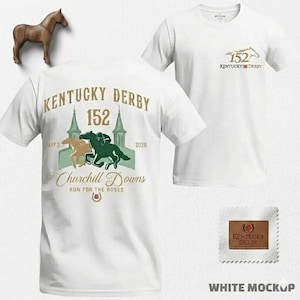 Op de afbeelding: Witte T-shirts met "Kentucky Derby 152" graphics. Eén shirt heeft een grote print op de rug met paarden en tekst, de andere een kleinere borstprint. Er is ook een houten paardenbeeldje aanwezig.